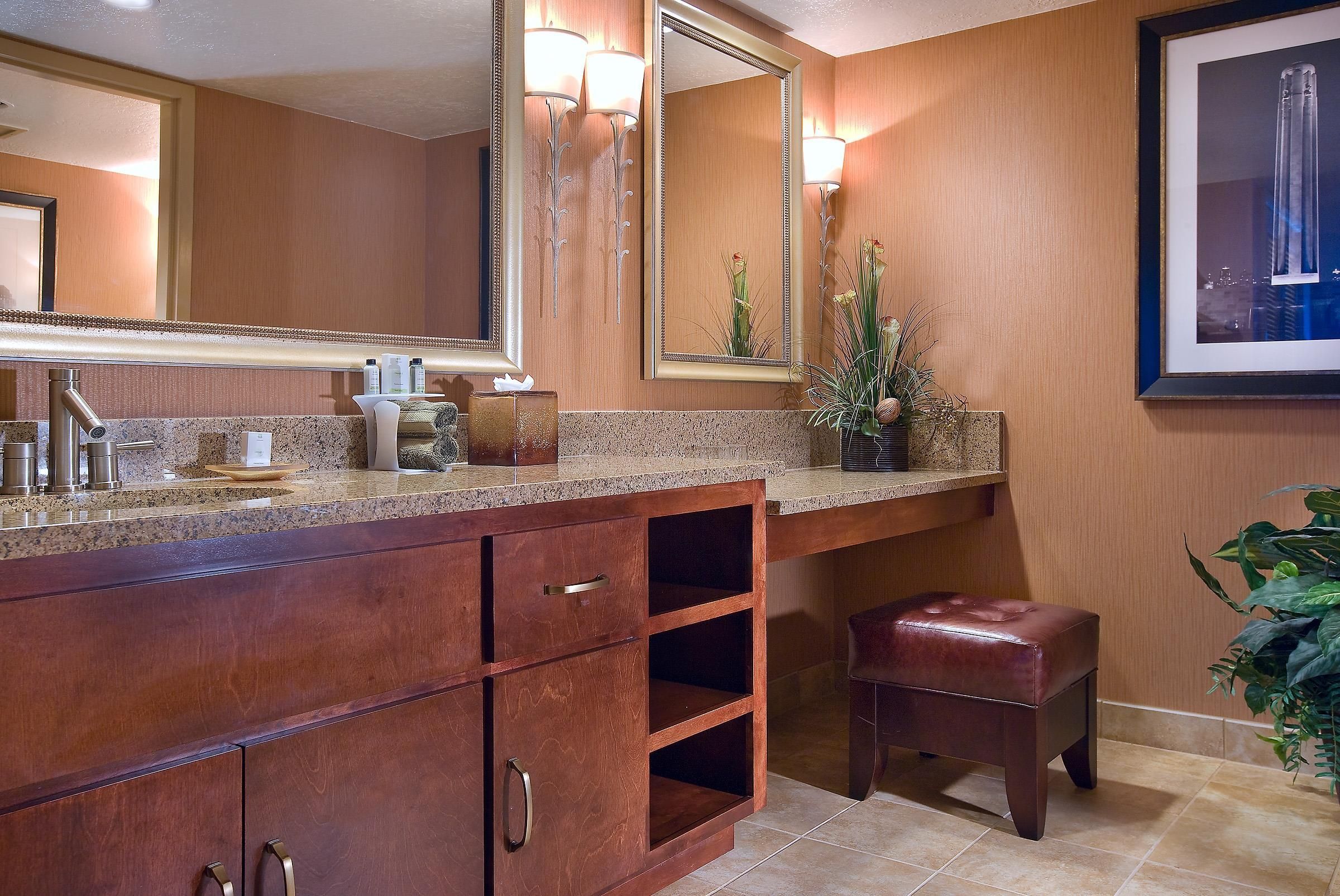 Une salle de bain dotée d’un comptoir en granit, d’un meuble-lavabo en bois, d’un grand miroir, d’un porte-serviettes et d’un tableau encadré au mur.
