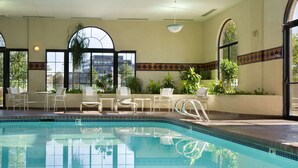 An indoor swimming pool with clear blue water, surrounded by white lounge chairs and potted plants. - Embassy Suites by Hilton Kansas City International Airport (Kansas City)
