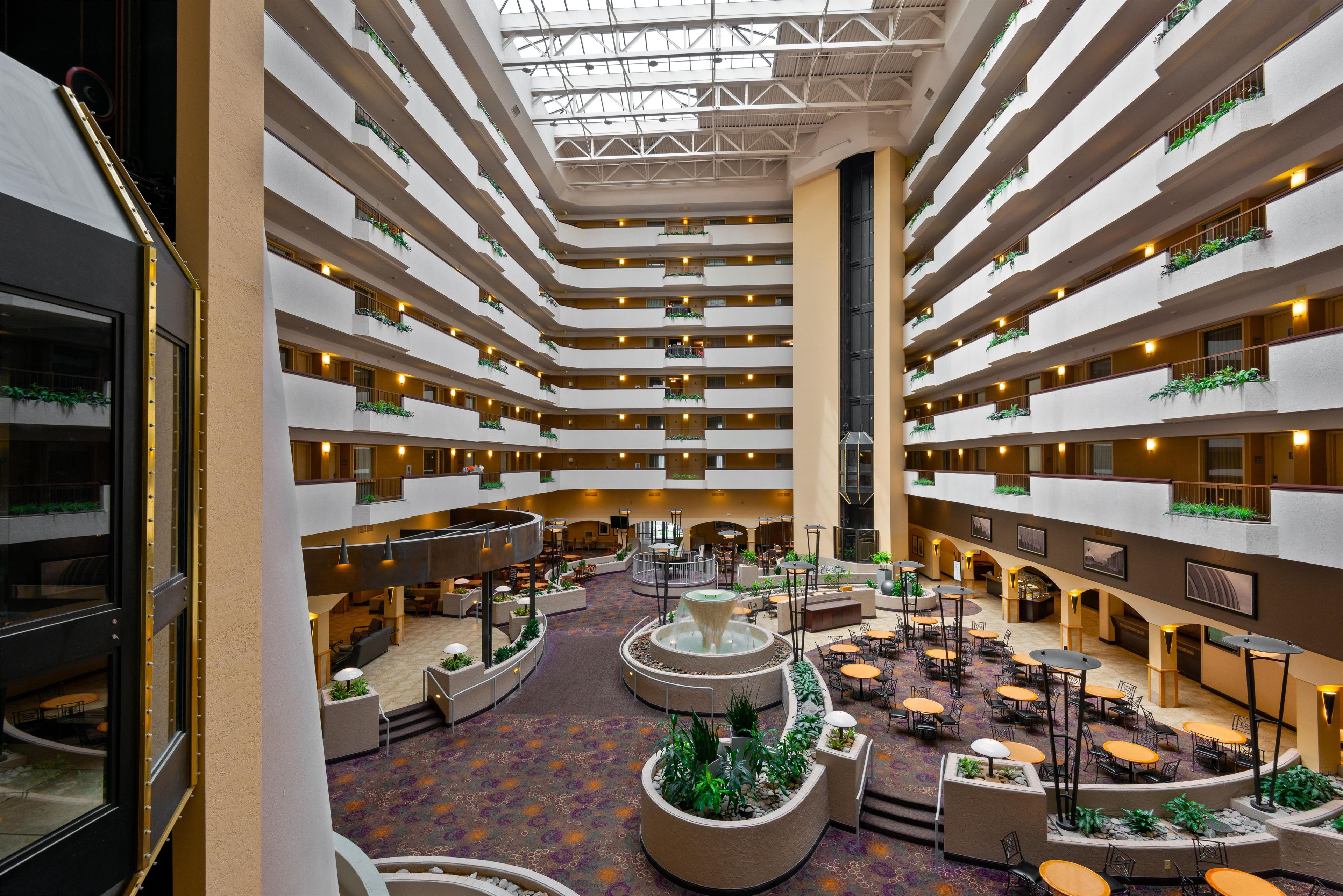A multi-level hotel atrium with a central water feature, multiple dining areas, and balconies with greenery.