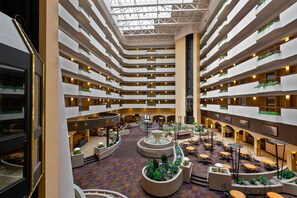 Ein mehrgeschossiges Hotel-Atrium mit einem zentralen Wasserspiel, verschiedenen Essbereichen und begrünten Balkonen.