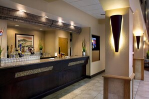 A hotel reception area with a bar, a framed landscape painting, and a television screen. - Embassy Suites by Hilton Kansas City International Airport (Kansas City)