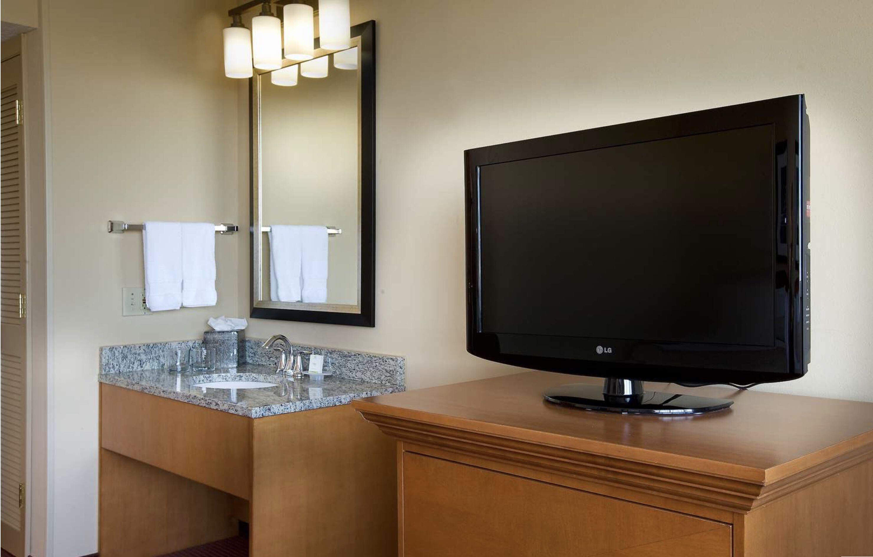 A bathroom with a granite sink, a mirror, and an LG flat-screen TV on a wooden cabinet.