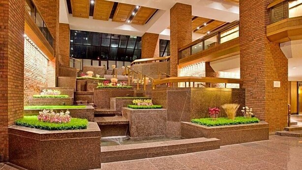 A spacious lobby with a central staircase, stone walls, and decorative planters with flowers. - Wyndham Gatineau-Ottawa & Conference Centre (Gatineau)