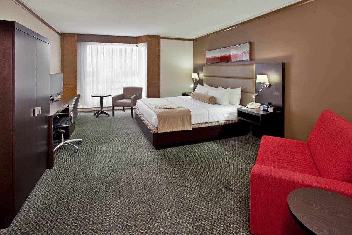 A hotel room with a bed, a desk, a chair, a red sofa, and a small table.