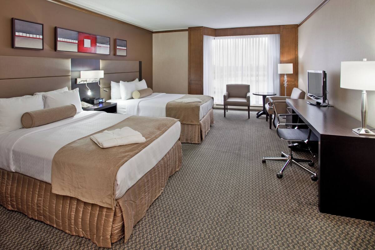 A hotel room with two beds, a desk, a chair, a TV, and a window with curtains.