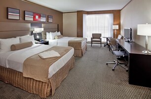 A hotel room with two beds, a desk, a chair, a TV, and a window with curtains.