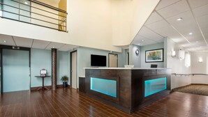 Un vestíbulo amplio con una recepción que cuenta con un panel azul iluminado, un televisor de pantalla plana grande y un cuadro en la pared.