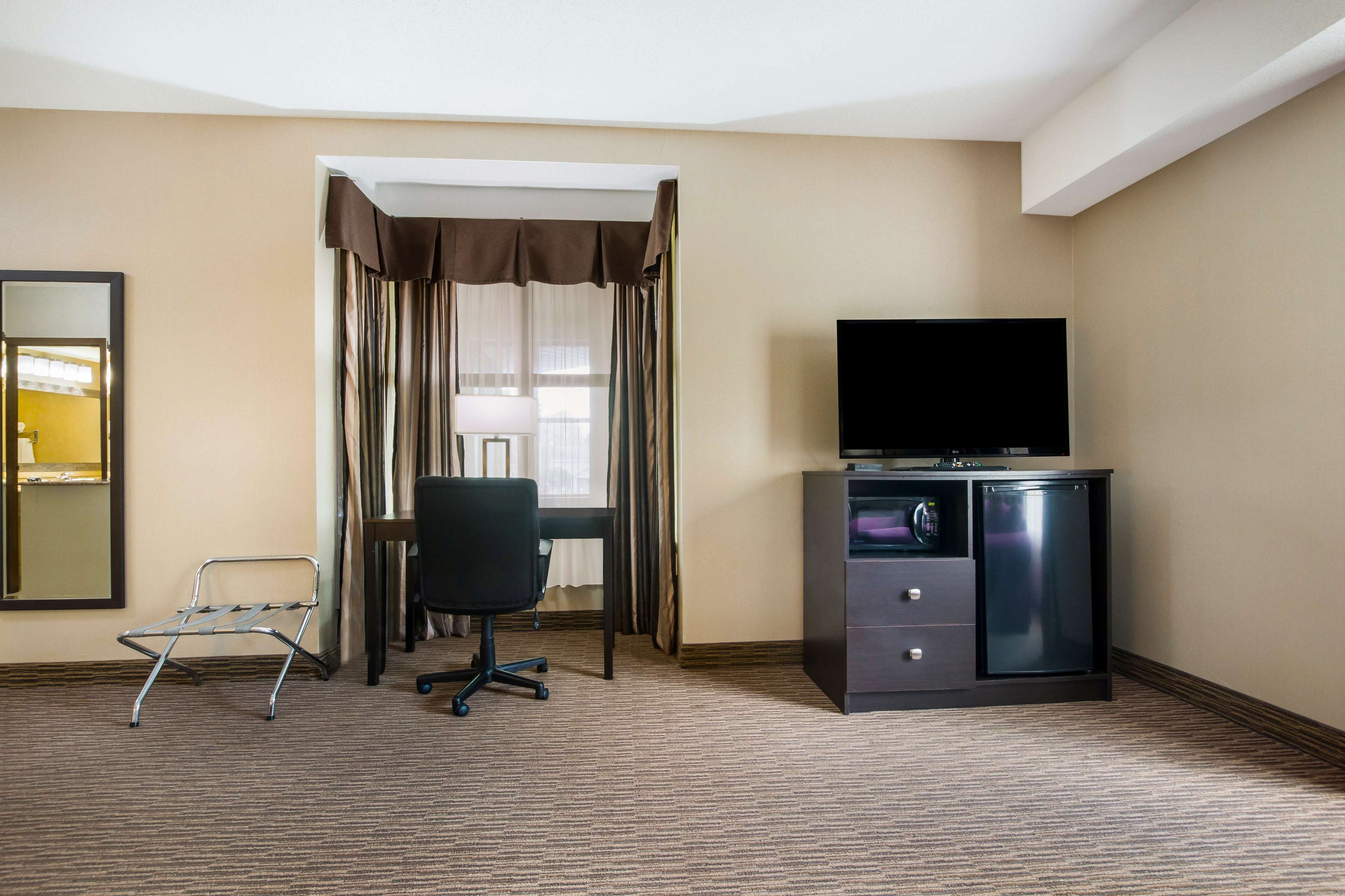 A hotel room with a bed, a desk with a television, a chair, and a minibar.