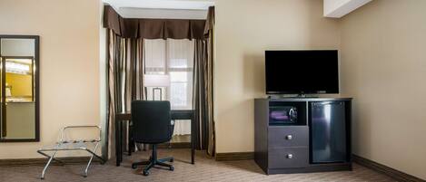 A hotel room with a bed, a desk with a television, a chair, and a minibar.