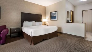 Habitación de hotel con una cama grande, una mesita de noche, una lámpara, una silla y un cuadro en la pared.