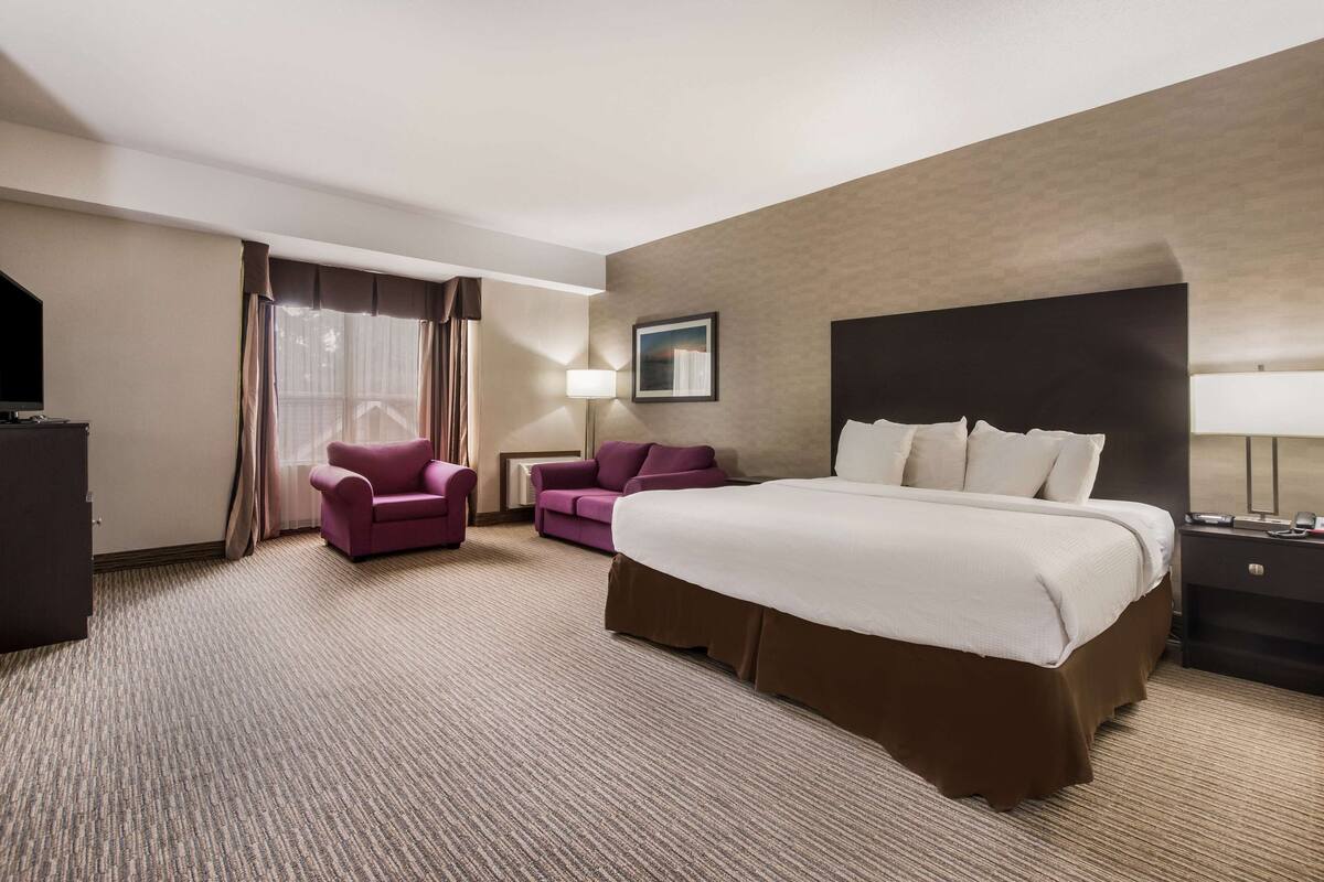 Una habitación de hotel con una cama grande, dos sillones, un escritorio y una televisión.