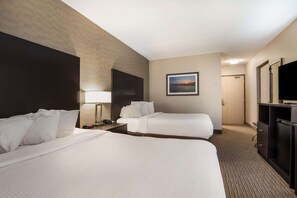 A hotel room with two beds, a TV, a desk with a lamp, and a painting on the wall.