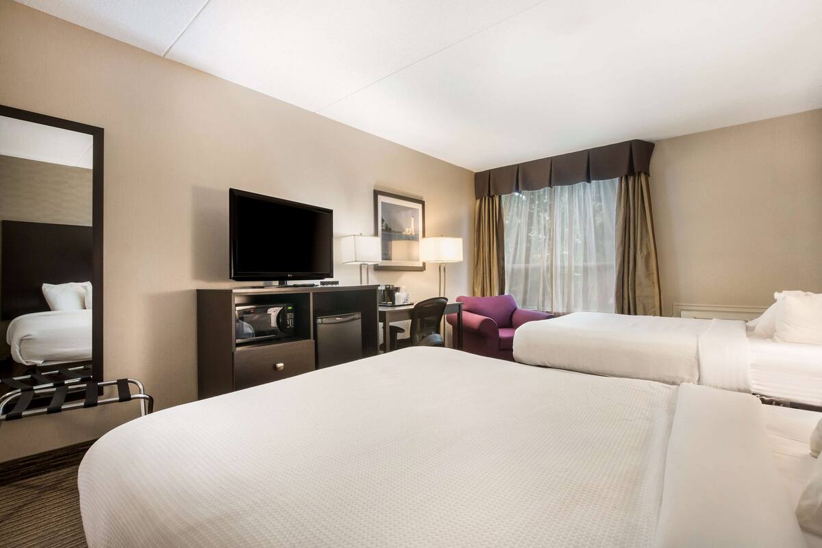 Una habitación de hotel con dos camas, un escritorio con televisor, una silla y un sillón morado.
