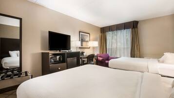 Quarto de hotel com duas camas, uma escrivaninha com televisão, uma cadeira e uma poltrona roxa.