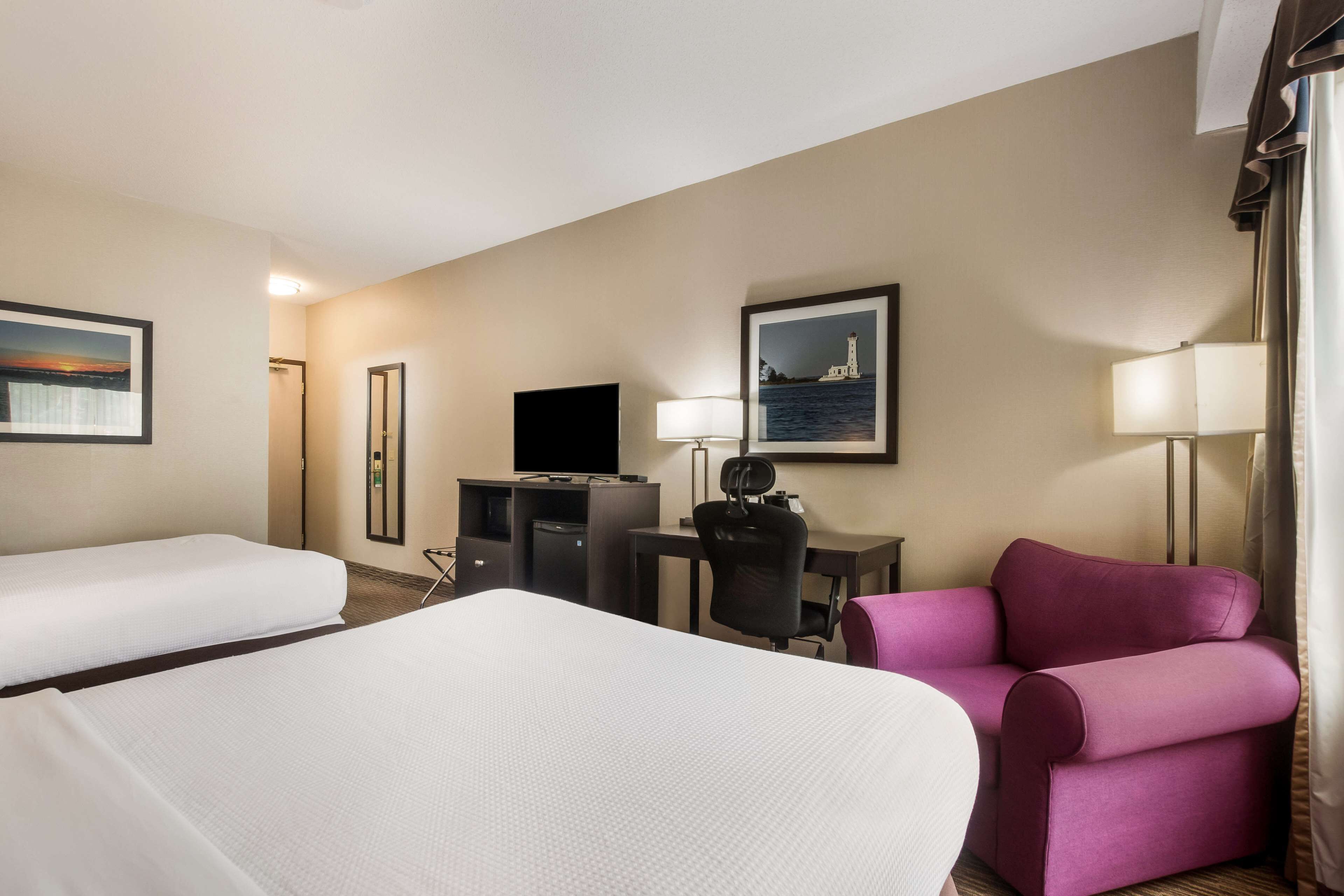 Une chambre d’hôtel avec deux lits, un bureau avec un ordinateur, une télévision et un fauteuil violet.