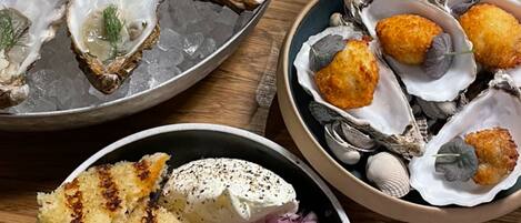 Diversos platos de mariscos, incluyendo ostras, opciones fritas y un bol con pan a la parrilla y cebollas.