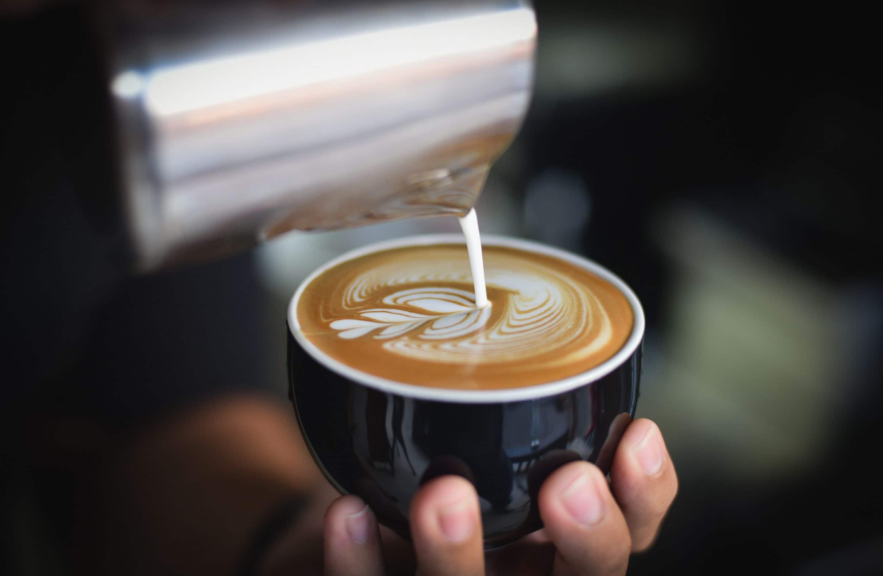 Uma mão segurando uma xícara de café com arte de latte.