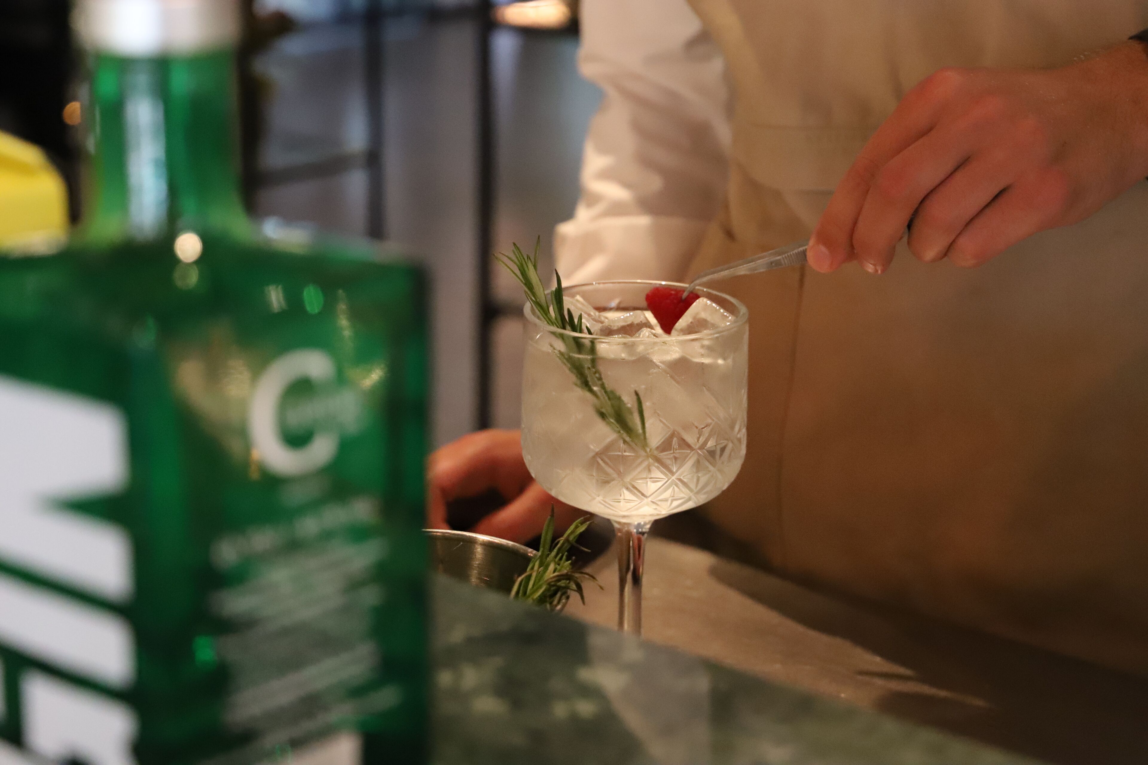 Une personne verse une boisson dans un verre contenant des glaçons et une branche de romarin.