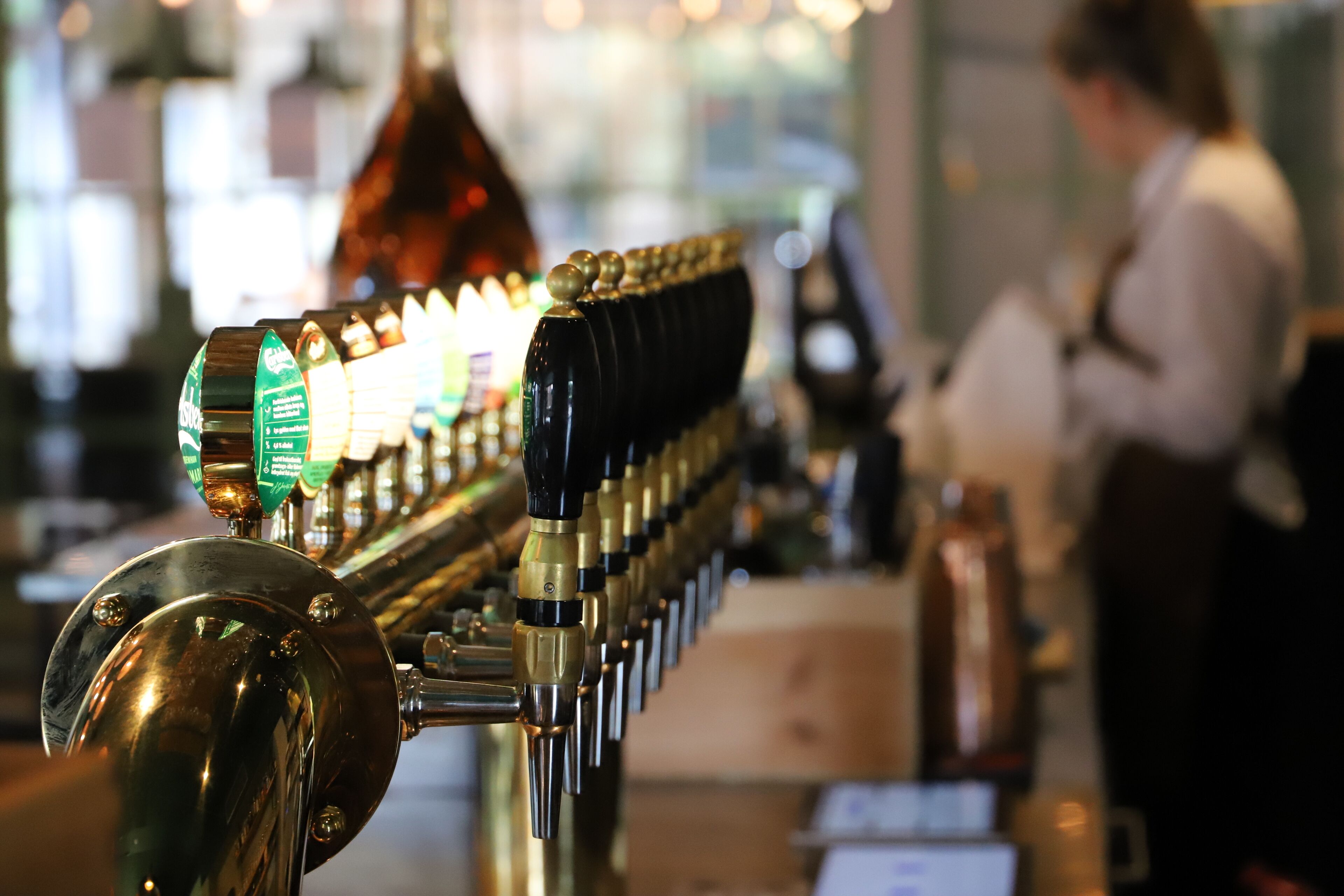 A bar with a row of taps and a person in the background.