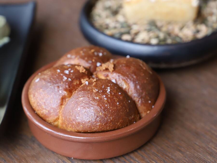 A loaf of bread in a brown bowl on a wooden table.