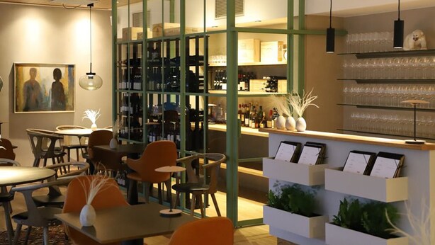 A cozy restaurant with a bar area, wooden tables, and chairs.