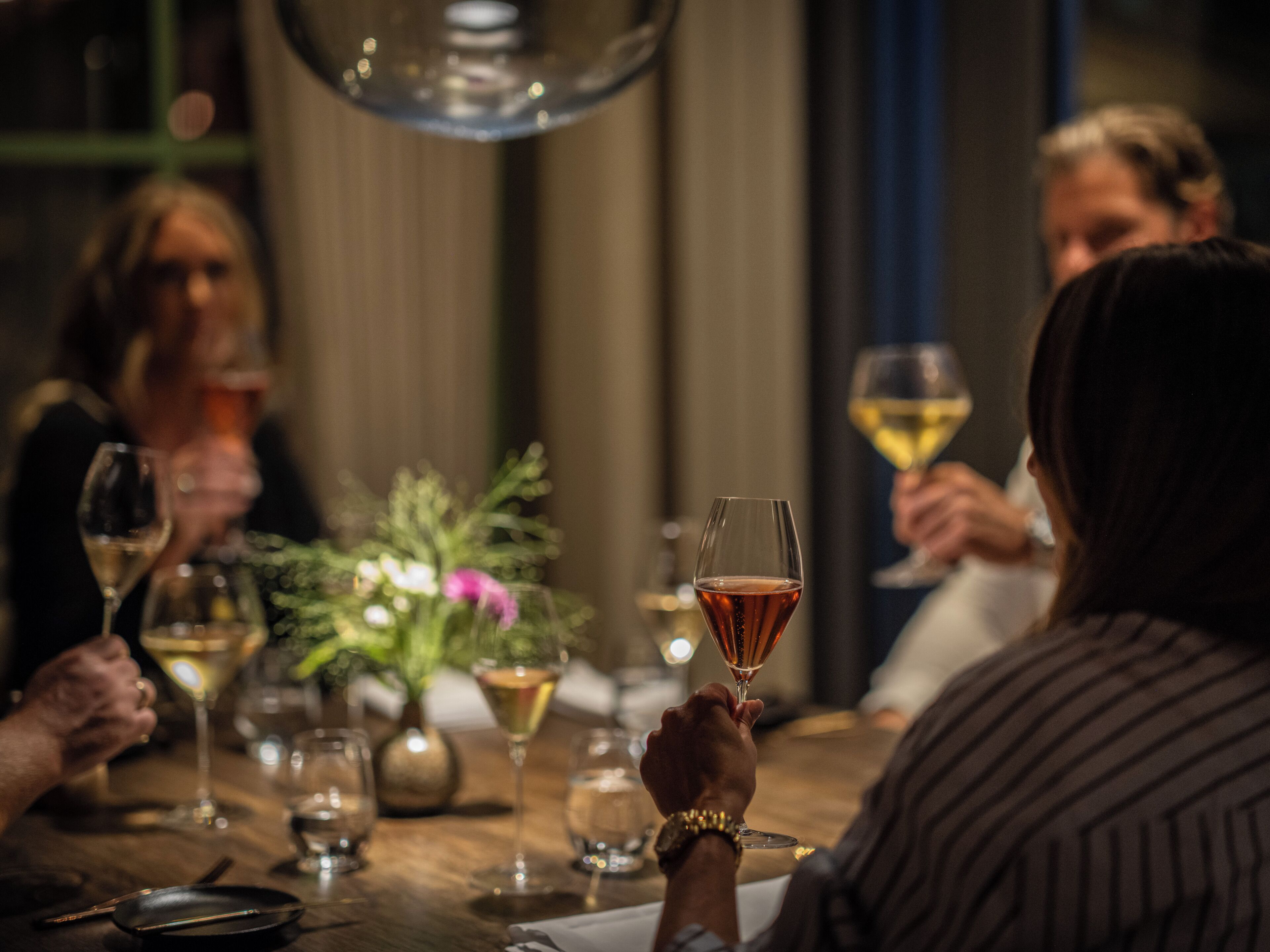 A group of people seated around a table with wine glasses, a vase with flowers, and a candle.