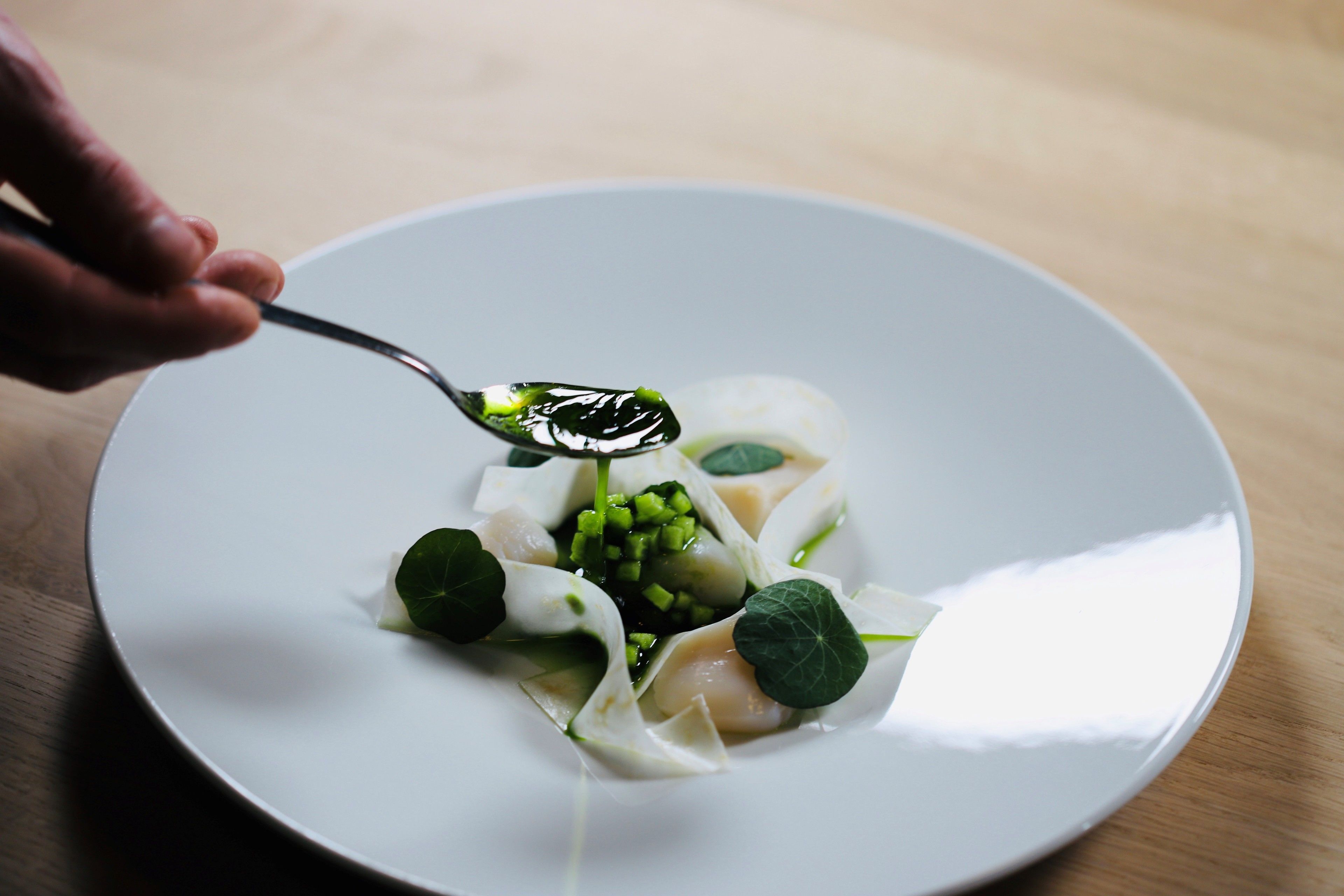 Une assiette blanche contenant une cuillère de nourriture, notamment des légumes verts et un liquide transparent.
