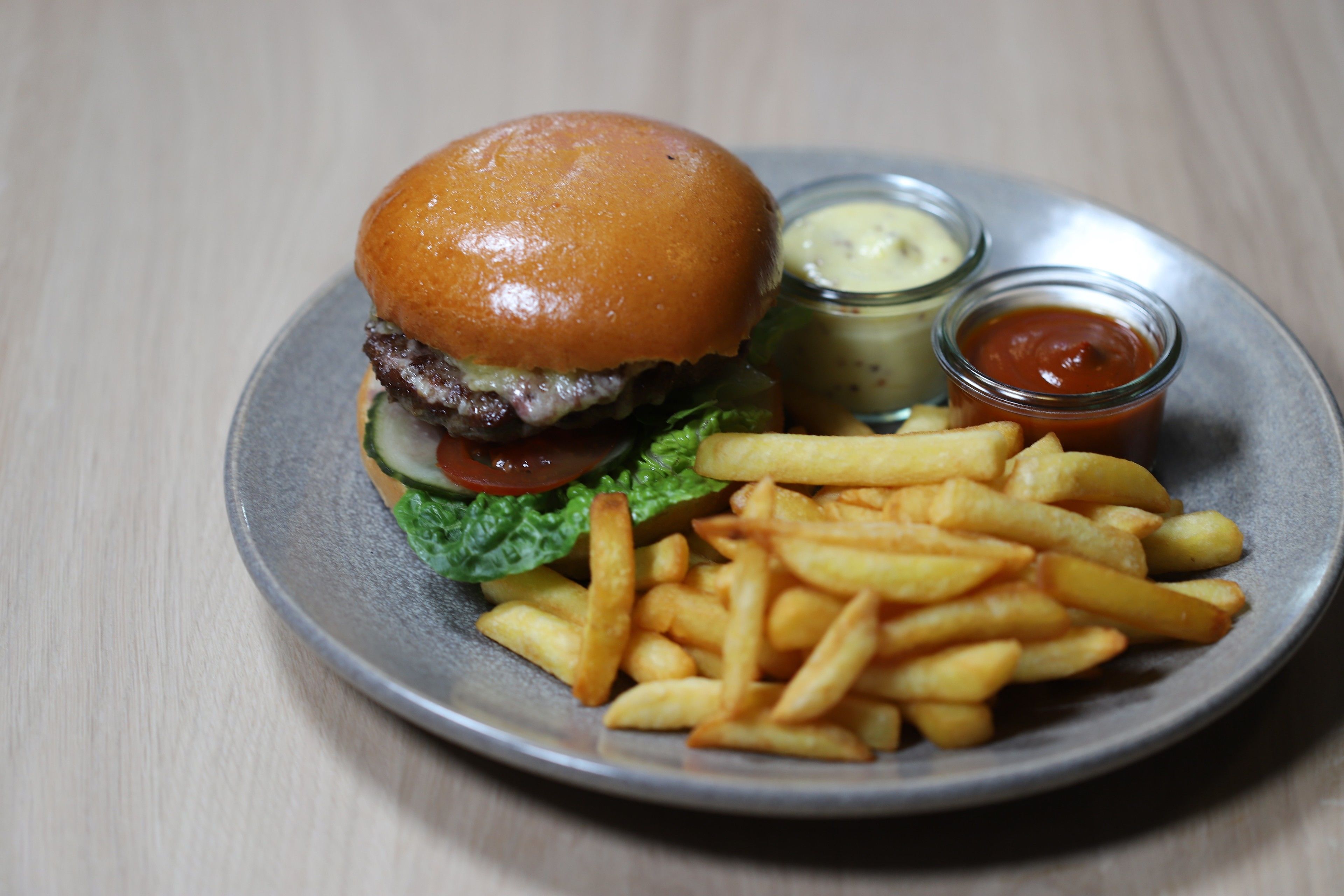 Un plato con una hamburguesa, papas fritas y dos salsas para mojar.