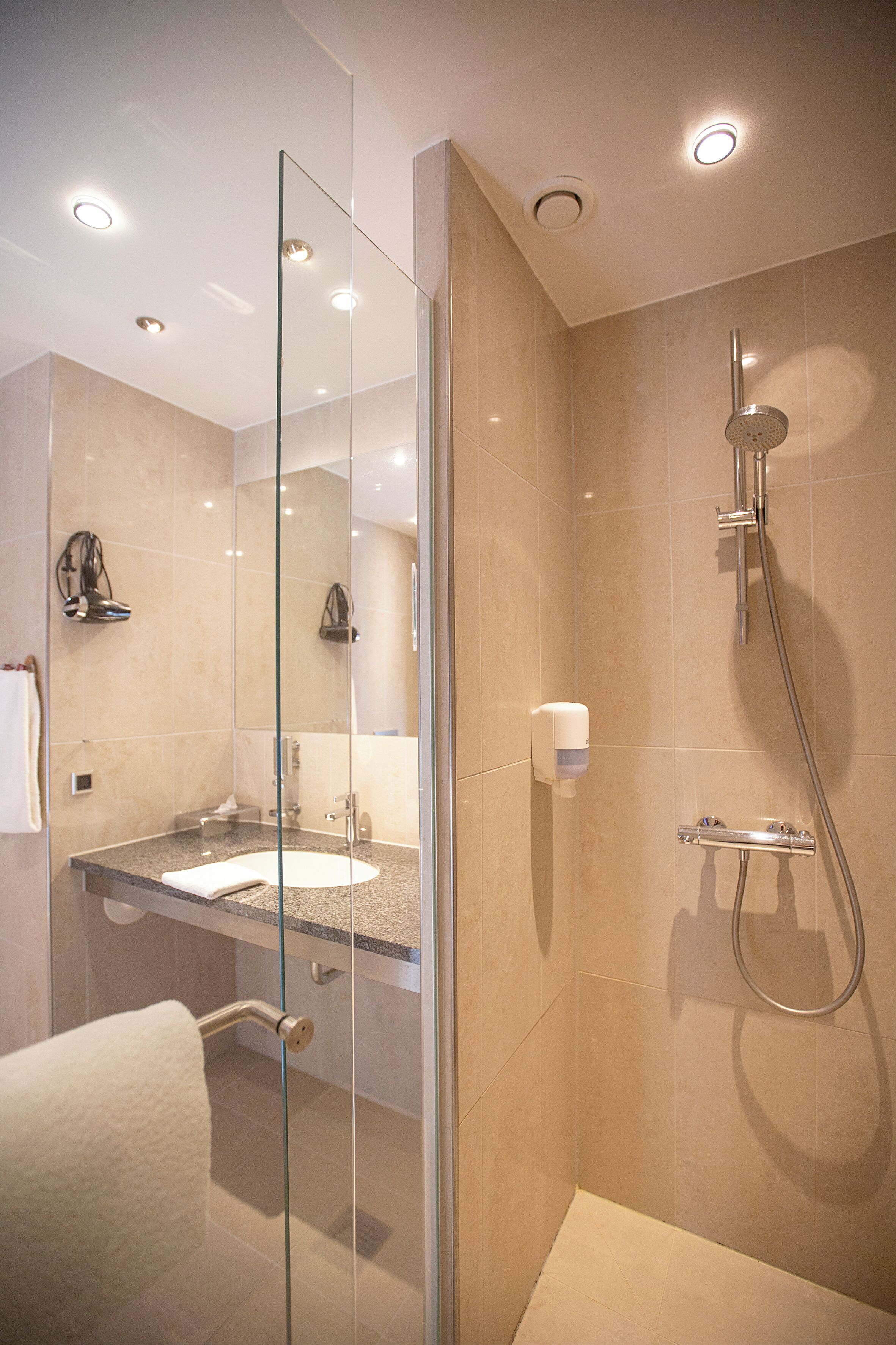 A modern bathroom with a glass shower enclosure, a sink with a towel, and a handheld showerhead.