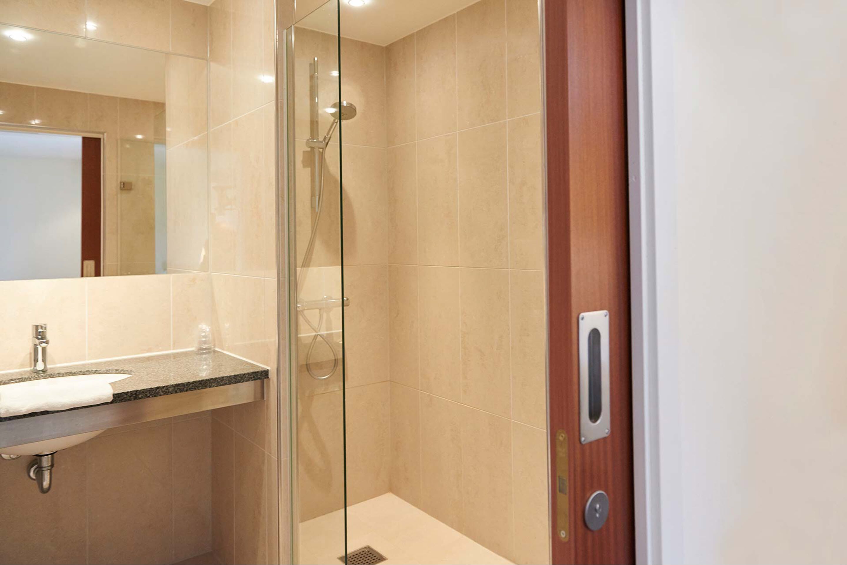 Un baño moderno con ducha acristalada, lavamanos con toalla y puerta de madera.
