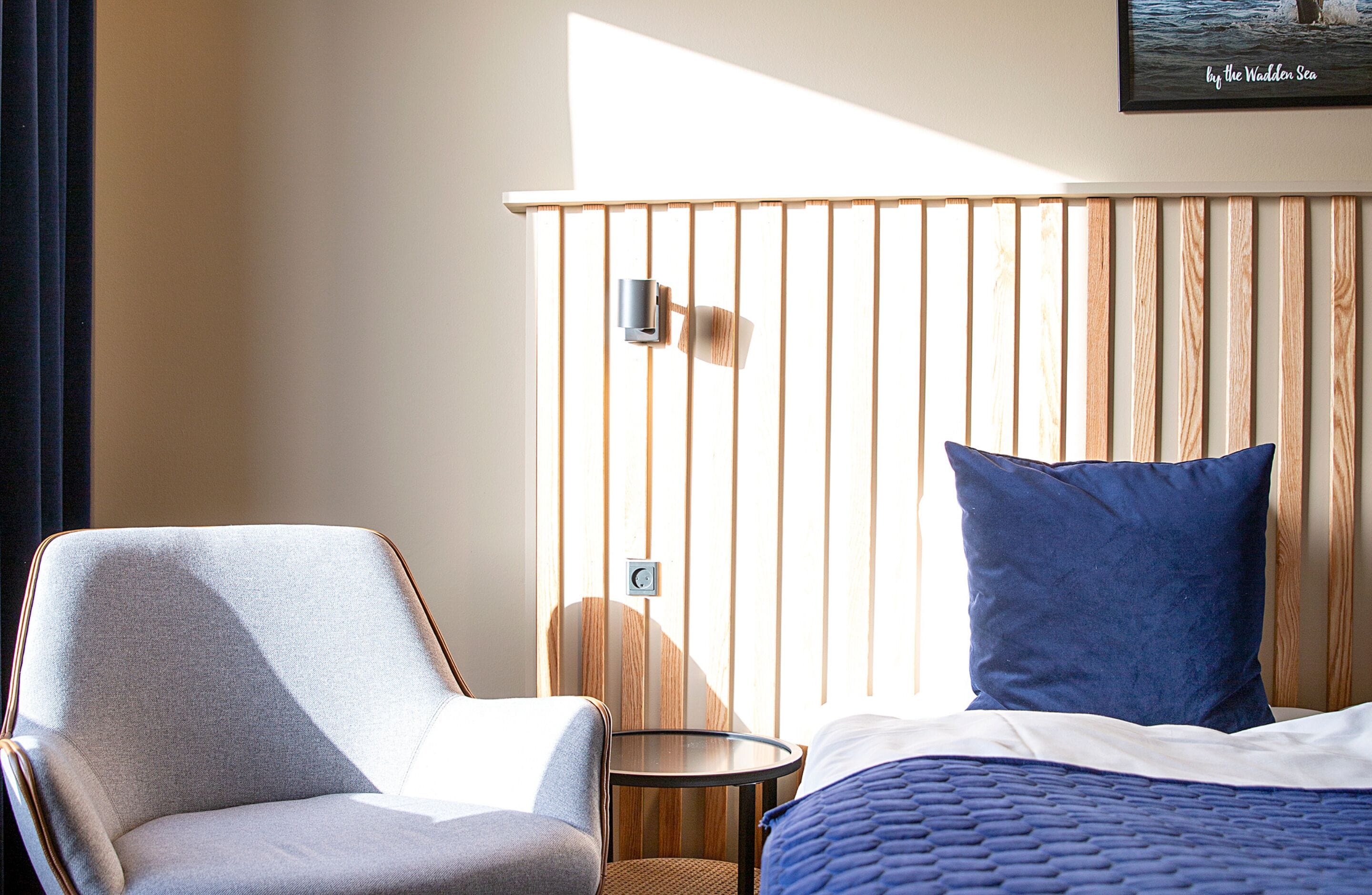 A hotel room with a bed, a chair, a small table, and a wooden slat wall.
