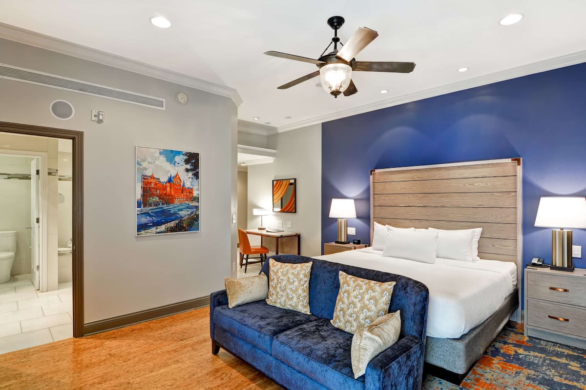 A hotel room with a large bed, a blue sofa, a ceiling fan, and a painting on the wall.