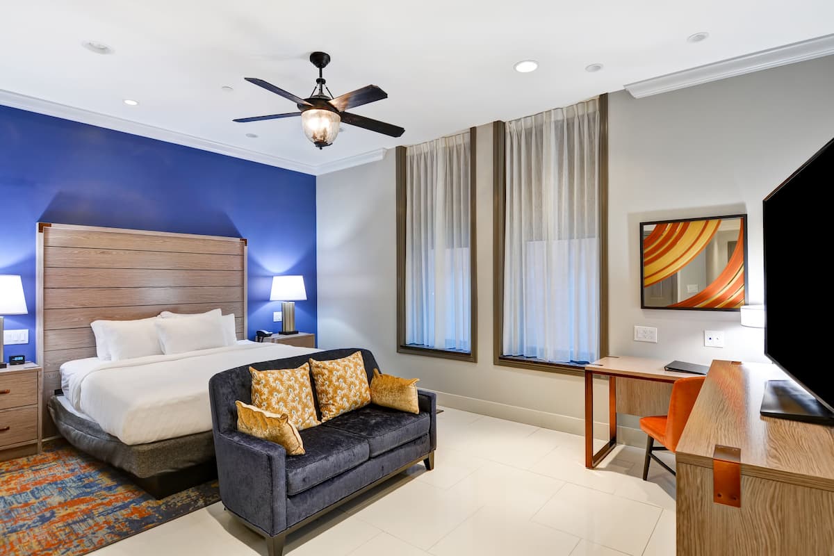 A hotel room with a bed, a sofa, a desk, and a ceiling fan.