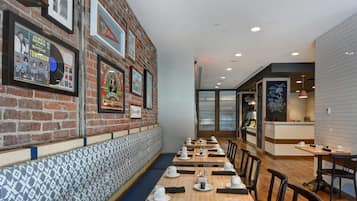 A restaurant with a brick wall, framed pictures, and a long counter with tables and chairs.