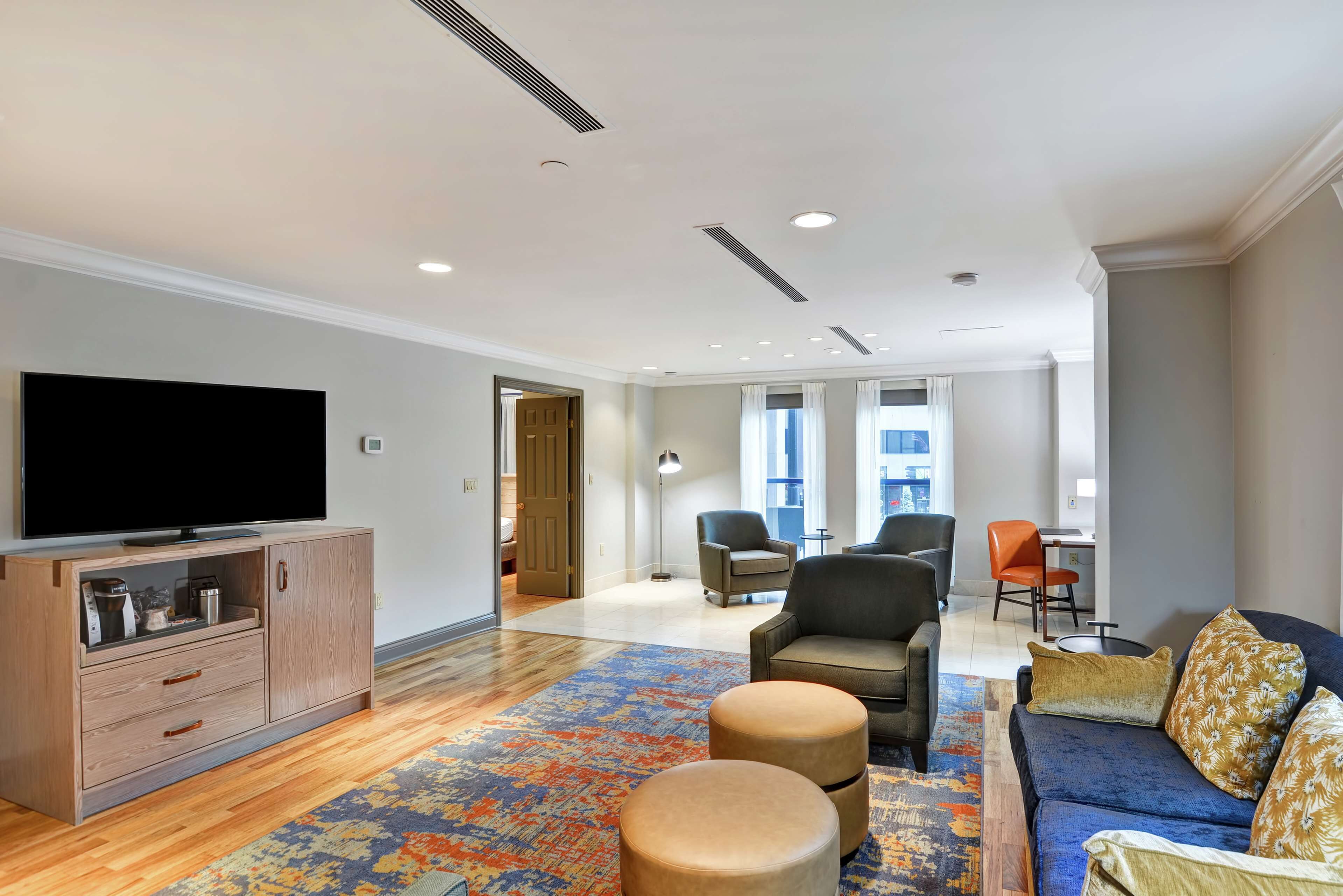 A modern living room with a flat-screen TV, a sofa, ottomans, and a patterned rug.