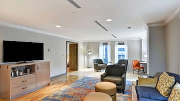 A modern living room with a flat-screen TV, a sofa, ottomans, and a patterned rug.