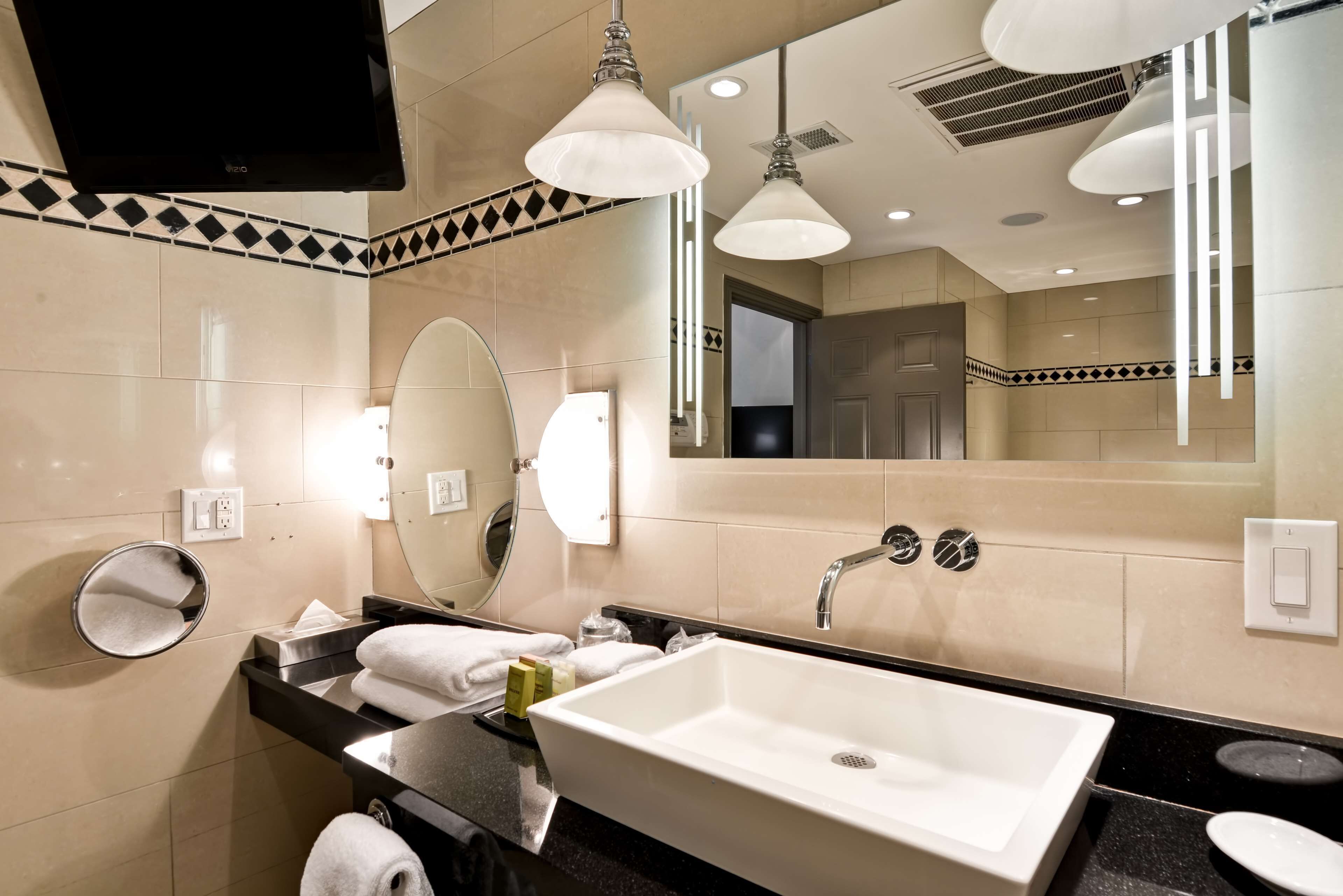 A modern bathroom with a large mirror, a sink with a faucet, and a television mounted on the wall.