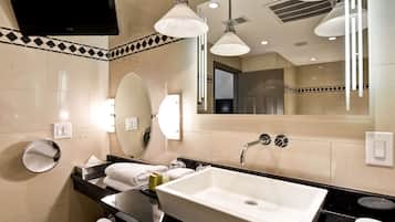 A modern bathroom with a large mirror, a sink with a faucet, and a television mounted on the wall.