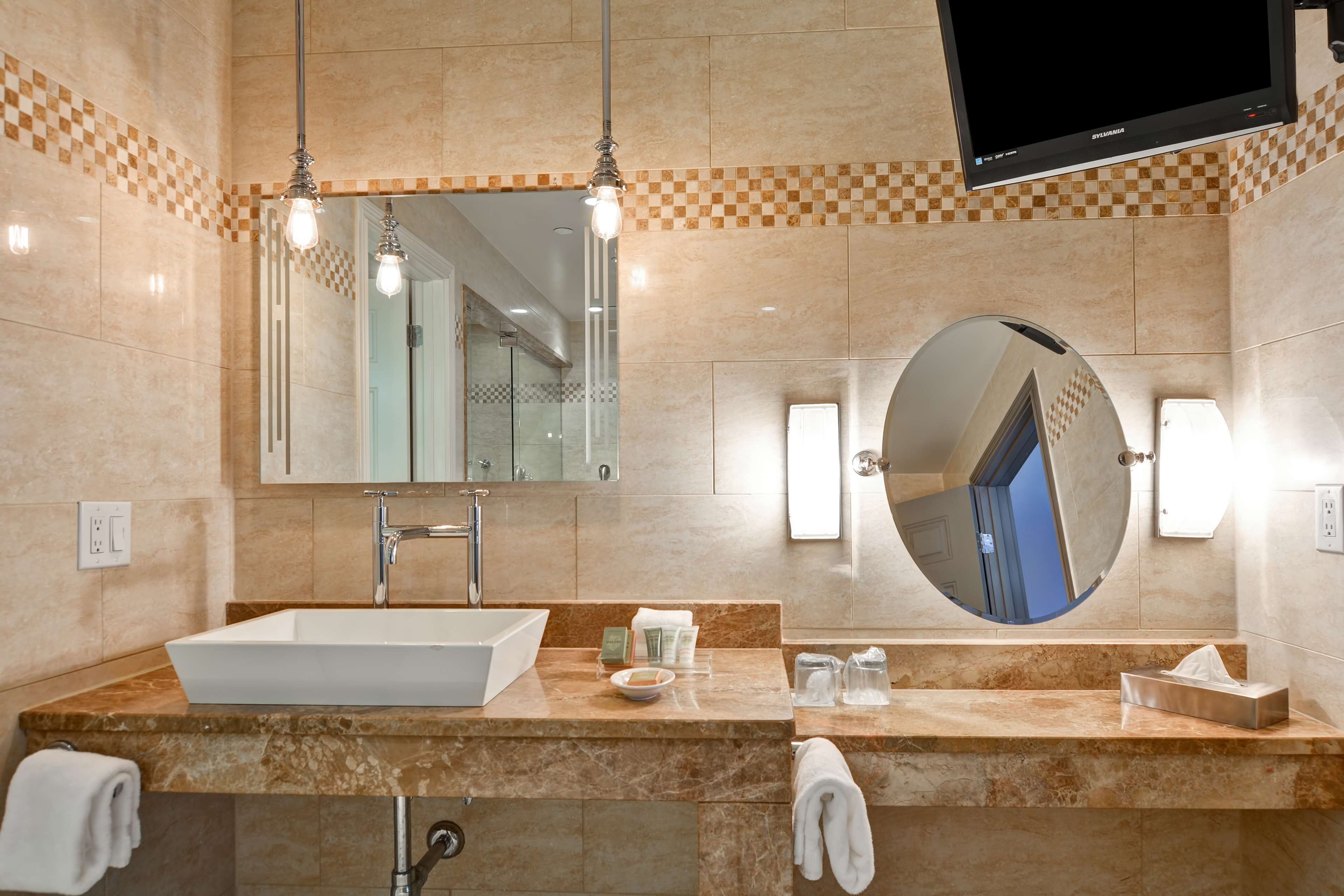 A modern bathroom with a large mirror, a sink, and a television mounted on the wall.