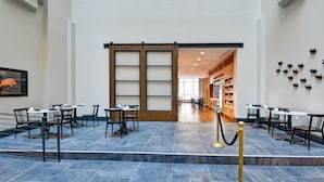 A spacious lobby with a modern design, featuring a central open area with tables and chairs, a wooden sliding door, and a staircase leading to an upper level. - The Cincinnatian Hotel Curio Collection by Hilton (Cincinnati)