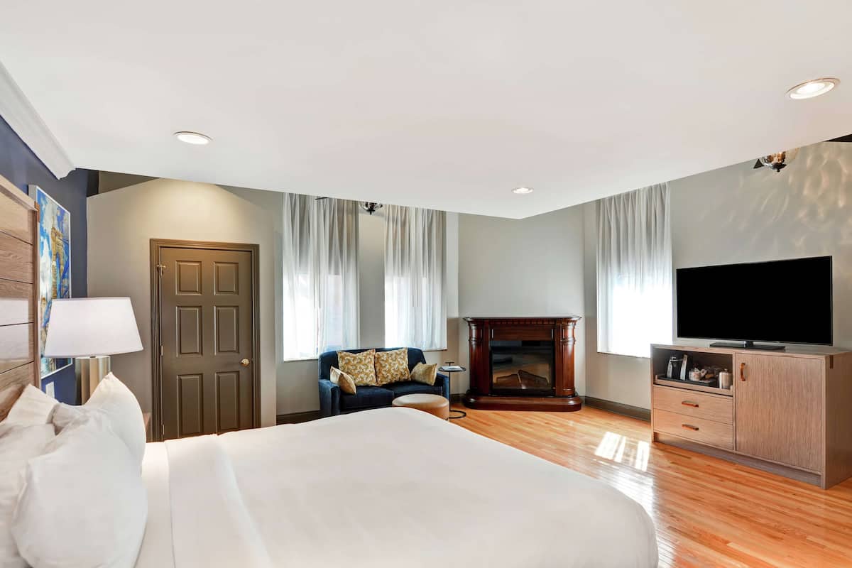 A hotel room with a large bed, a television, a fireplace, and a wooden cabinet.
