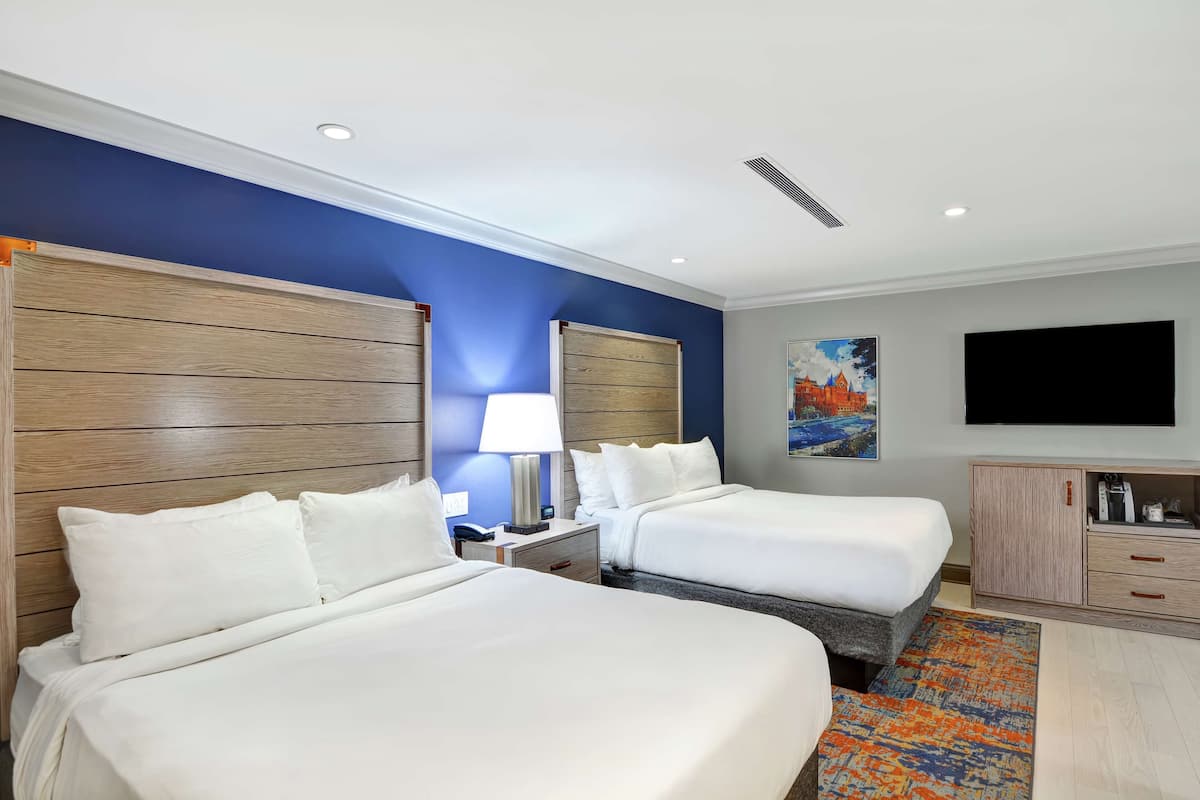 A hotel room with two beds, a nightstand with a lamp, a TV, and a cabinet.