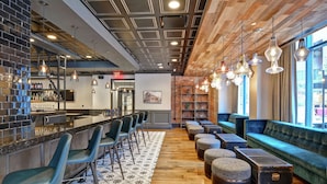 A bar area with stools, a counter, and a seating area with sofas and ottomans. - The Cincinnatian Hotel Curio Collection by Hilton (Cincinnati)
