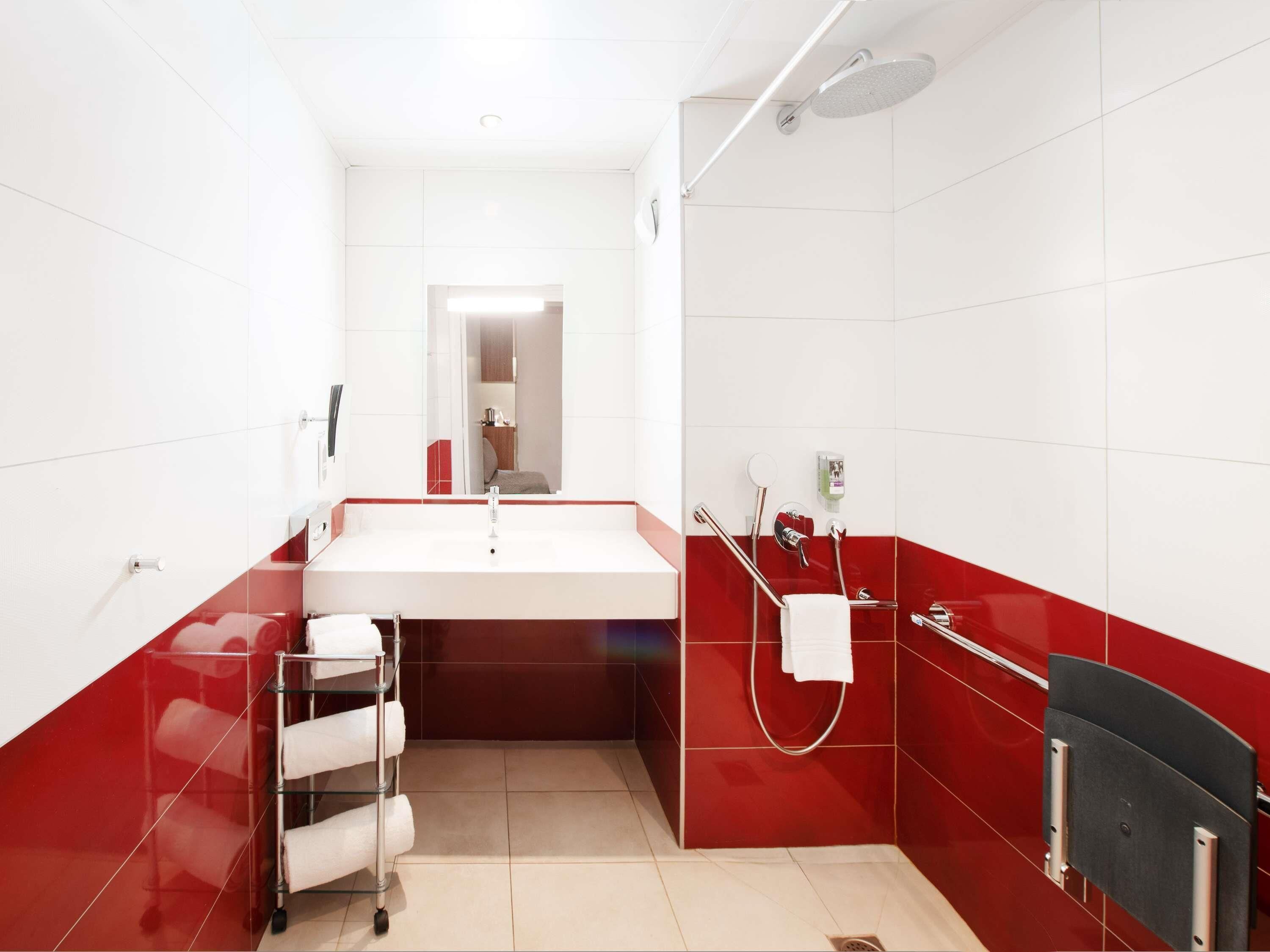 Un baño moderno con un lavabo blanco, paredes con azulejos rojos, una cabina de ducha de vidrio y un perchero para toallas.