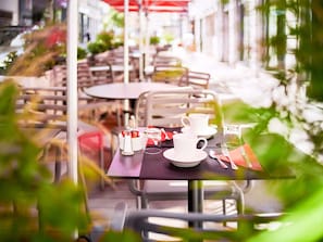 Een terras met tafels en stoelen, en een rode parasol.