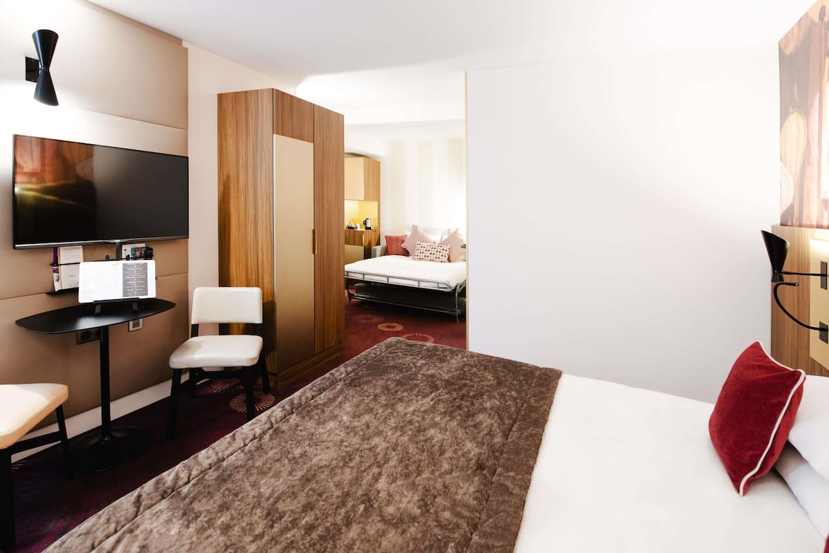 Ein Hotelzimmer mit einem Bett, einem Schreibtisch mit Computer, einem Fernseher und einer Sitzecke mit Stühlen.