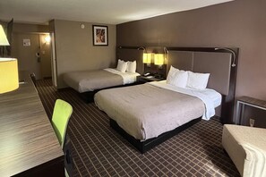 Hotellihuone, jossa on kaksi sänkyä, työpöytä, tuoli ja yöpöytä, jossa on lamput.