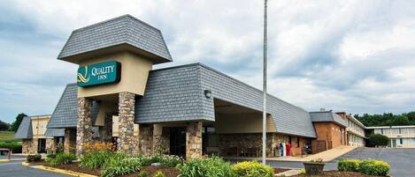 A Quality Inn hotel with a stone facade, a flagpole with an American flag, and a landscaped entrance.