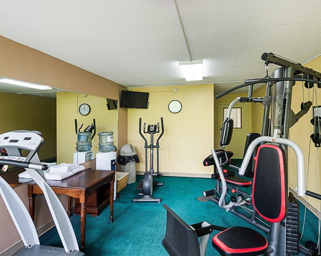 Een sportschool met trainingsapparatuur, een bureau en een waterkoeler.