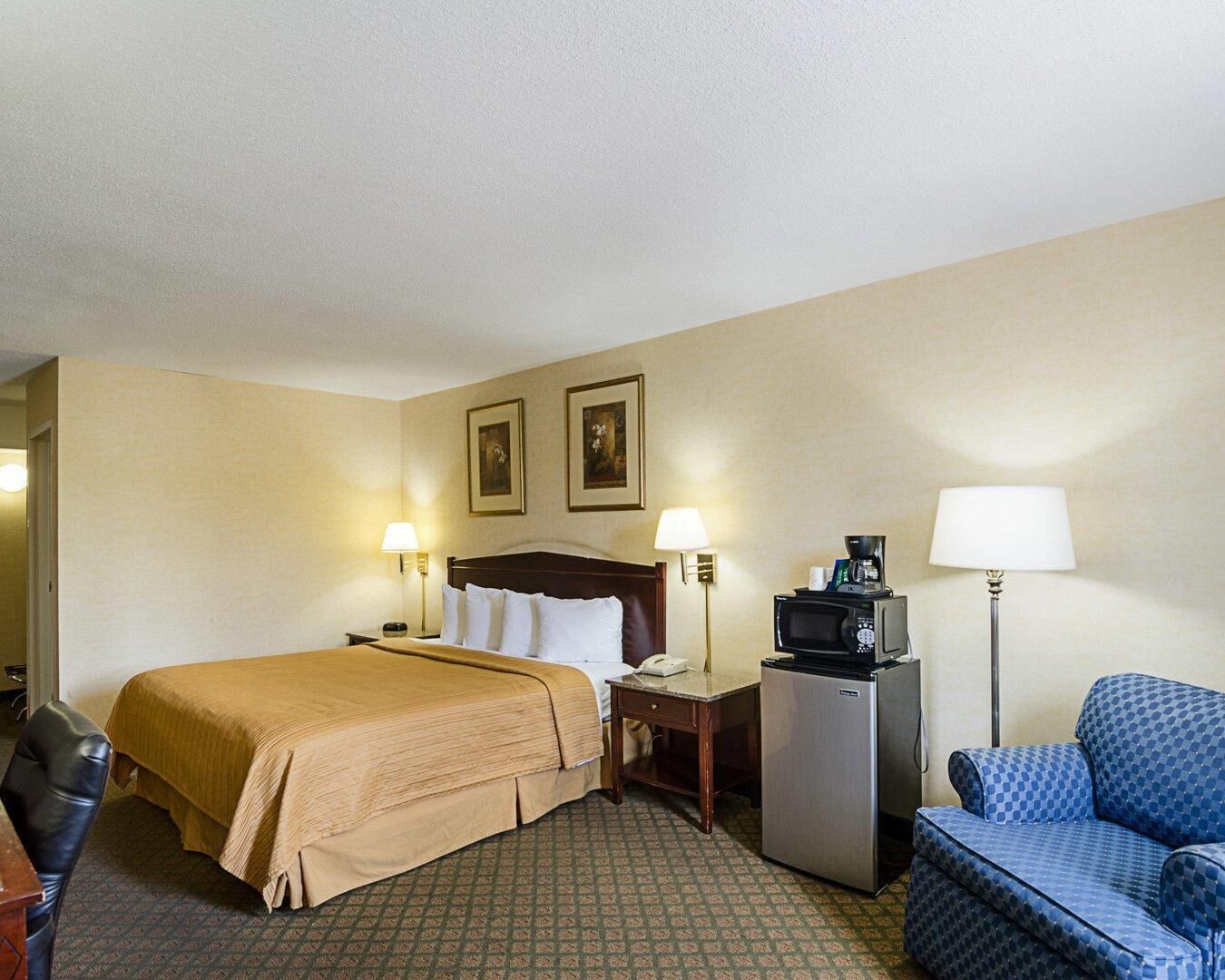 Een hotelkamer met een bed, een bureau, een stoel, een koelkast en een magnetron.